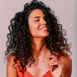 Mulher com cabelos cacheados pegando em seus fios de cabelo